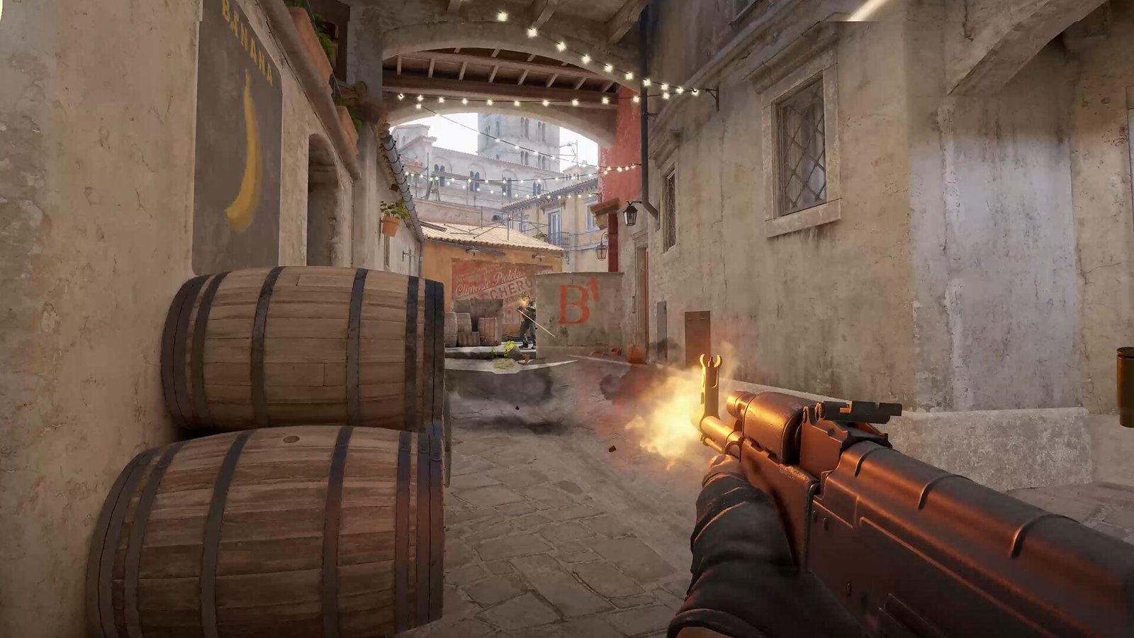 Rifle disparando en primera persona por un pasaje con barriles y la marca del sitio B en Counter-Strike 2 (2023).